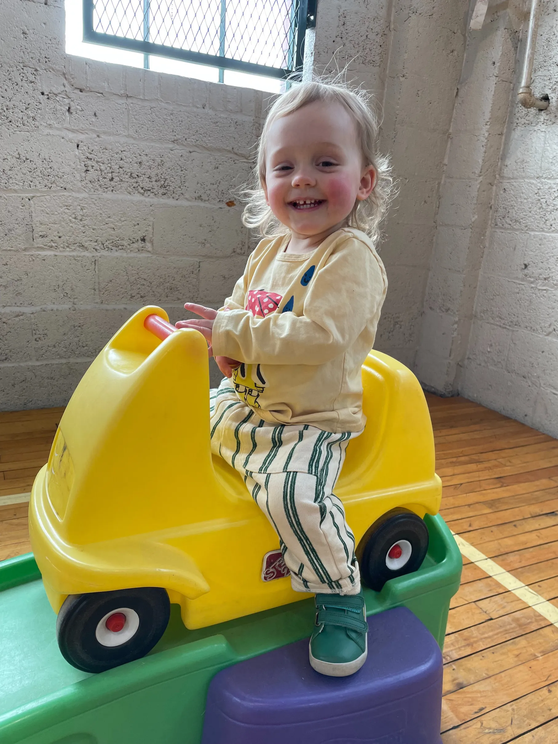 Picture of a smiling two-year old girl sitting on a roller coaster toy at Tot Spot Lancaster.